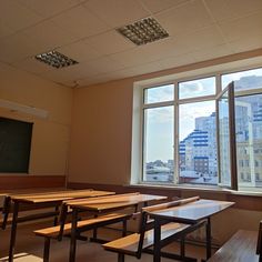 an empty classroom with desks and a chalkboard in front of a window overlooking the city