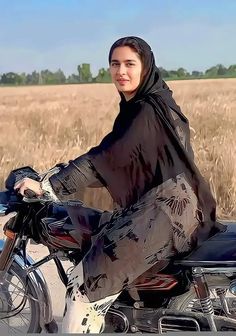 a woman sitting on the back of a motorcycle in front of a field with wheat