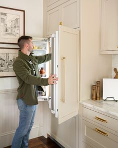 a man standing in front of an open refrigerator with the door ajar and looking inside