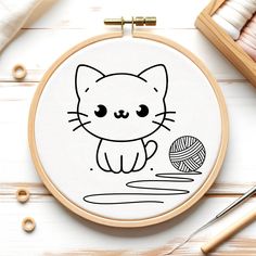 an embroidery kit with a cat and ball of yarn on the table next to it