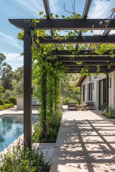 an outdoor covered patio next to a swimming pool with greenery on the pergoline