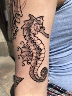 a woman's arm with a black and white seahorse tattoo on it