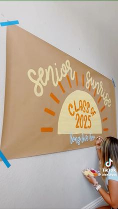 a girl is painting on the wall with her name and class year sign in front of her