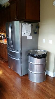 a metallic refrigerator freezer sitting next to a trash can on top of a hard wood floor