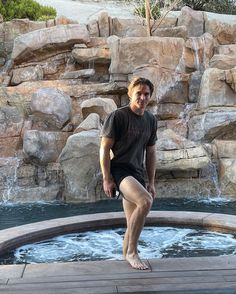 a man sitting on the edge of a hot tub in front of a rock waterfall