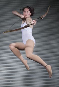 a woman in white leotard holding a bow and arrow with her right hand