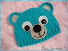 a crocheted blue bear hat with big eyes on top of a pink blanket