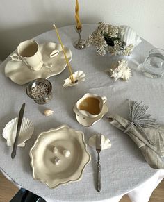 a table topped with dishes and cups filled with condiments on top of a white table cloth