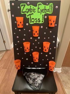 a black and orange board with plastic cups on it that says zombie eyeball toss