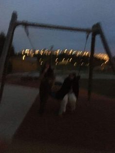 two children playing on a swing set at night