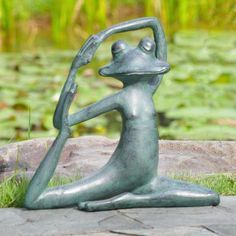 a statue of a frog sitting on the ground with its arms in the air holding a plant