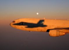 an airplane is flying in the sky at sunset with its shadow on the wing and moon behind it