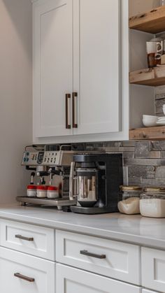 a coffee maker sitting on top of a counter next to white cupboards and drawers