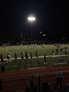 a football game is being played on the field at night with people watching from the sidelines