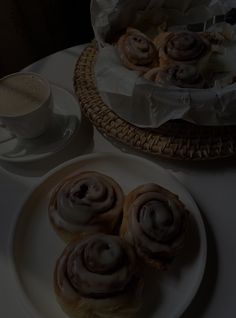 some pastries are on a white plate next to a cup of coffee and a wicker basket