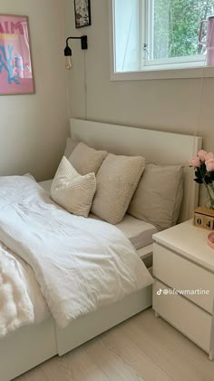 a white bed sitting in a bedroom next to a dresser with flowers on top of it