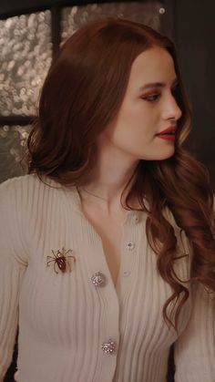 a woman with long brown hair wearing a white shirt and red lipstick is standing in front of a window