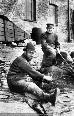 two men sitting on the ground with fishing nets in their hands and one man standing next to them