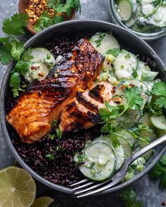 a bowl filled with black rice, cucumber and salmon on top of it