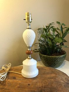 a white lamp sitting on top of a wooden table next to a potted plant