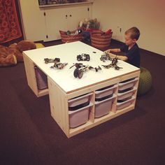 a young boy sitting on the floor in front of a white table with bins