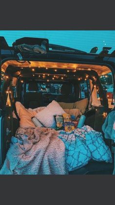 the back end of a van filled with blankets and pillows covered in fairy lights at night