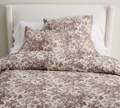 a bed covered in purple and white floral print sheets with pillows on top of it