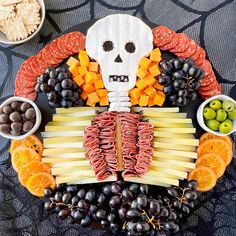 a skeleton made out of cheese, fruit and meats on a platter with olives