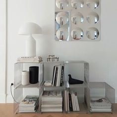 a shelf with books and magazines in front of a mirror on the wall above it