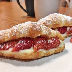 two pastries with strawberries on them sitting on a plate next to a cup