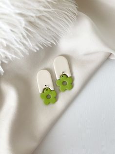 two green and white flower shaped earrings sitting on top of a white cloth covered surface