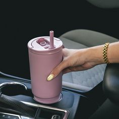 a woman is holding a pink cup in her car