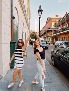 two women standing on the sidewalk with their arms in the air