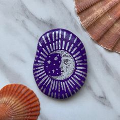 two seashells and a purple plate on a marble surface with the moon painted on it