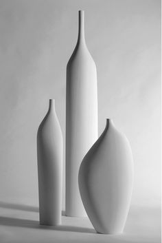 three white vases sitting next to each other in front of a gray background,