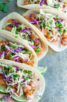 four fish tacos with cole slaw, lime and cilantro on top