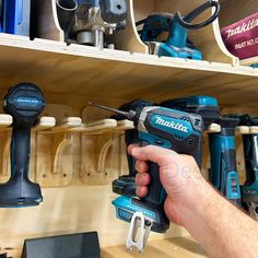 a man is holding a driller in his hand and some tools are on the shelves behind him