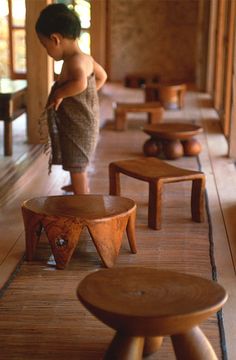 a little boy standing in front of wooden stools on the floor next to each other