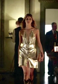 a woman in a gold dress and cowboy boots walking down a hall with other people