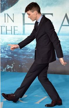 a man in a suit and tie walks on the blue carpet with his hand out