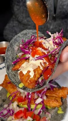 a person pouring sauce on some food in a tortilla shell with coleslaw and other toppings