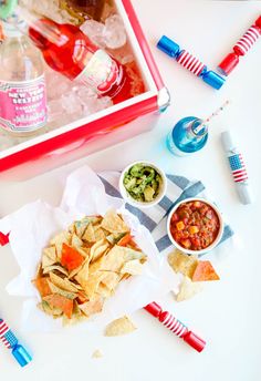 a table with chips, salsa and sodas on it next to an ice box