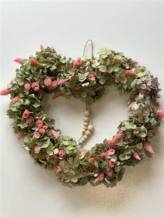 a heart shaped wreath with pink flowers and greenery hanging from the side on a wall