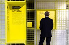 a man standing in front of a yellow display case with words on the wall and behind it