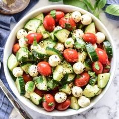 a white bowl filled with cucumber, tomatoes and basil on top of a marble table