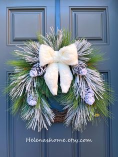 a christmas wreath with pine cones and white fur is hanging on a blue door frame