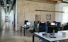 an office filled with desks and computers in front of a brick wall that has exposed beams