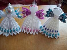 three paper angel ornaments sitting on top of a wooden table