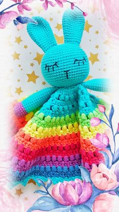 a crocheted stuffed rabbit sitting on top of a rainbow colored blanket with stars in the background