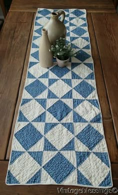 a blue and white quilted table runner on a wooden table with two vases